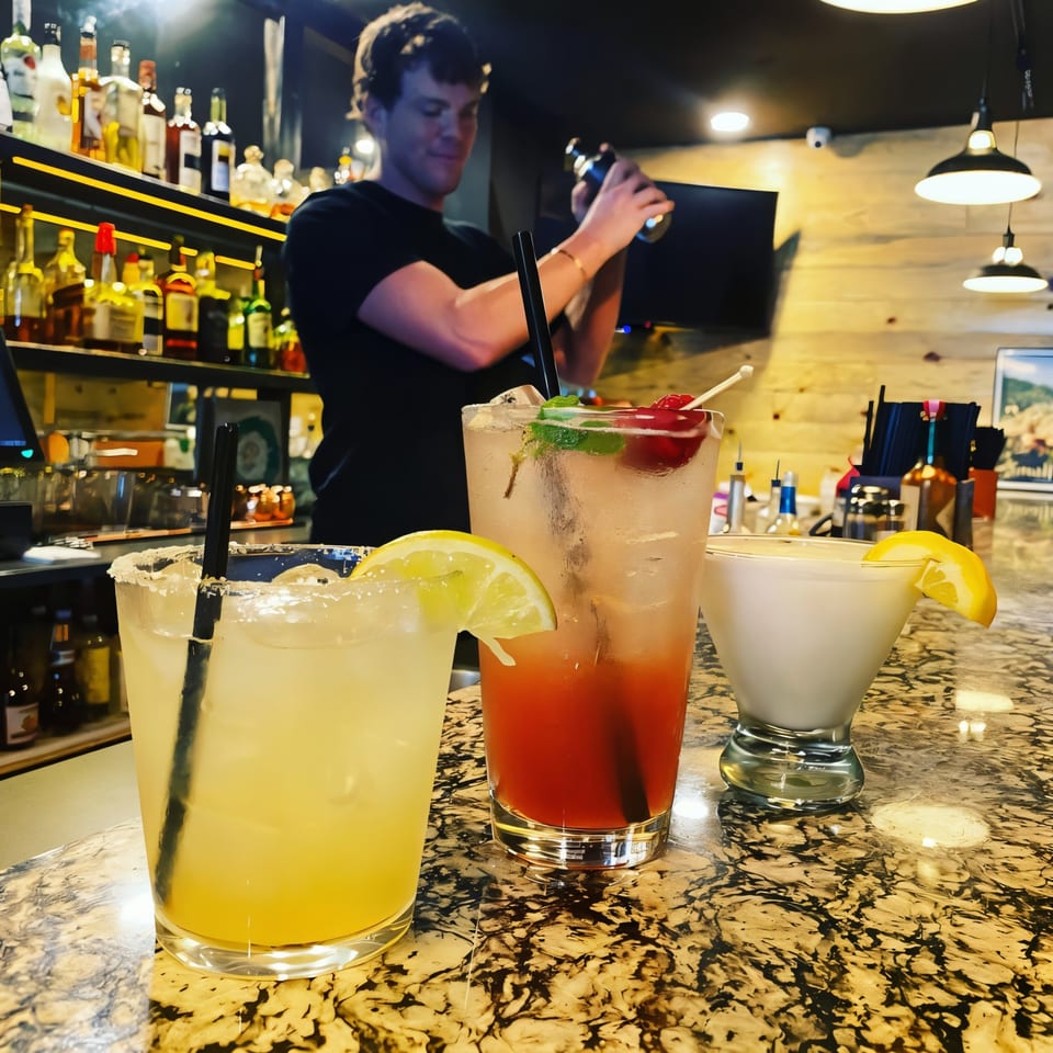 Bartender shaking a cocktail behind a bar with three drinks on the counter at Pacioni's Pizzeria.