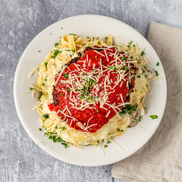 Chicken Parmesan with fettuccine Alfredo, topped with marinara, shredded cheese, and parsley.