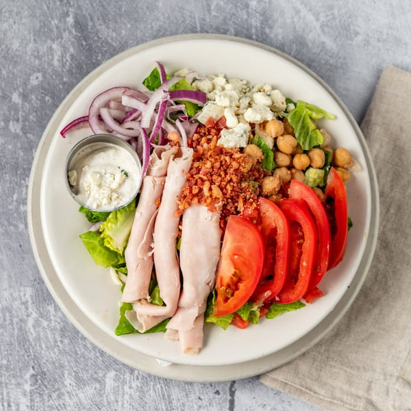 A vibrant Pacioni's Pizzeria salad with turkey, bacon, tomatoes, chickpeas, red onion, and blue cheese.