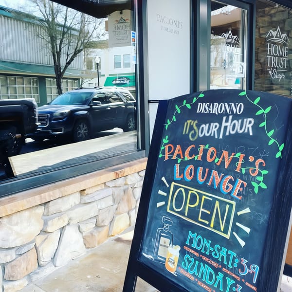 A Pacioni's Pizzeria chalkboard sign advertises "It's Our Hour" and lounge opening times.