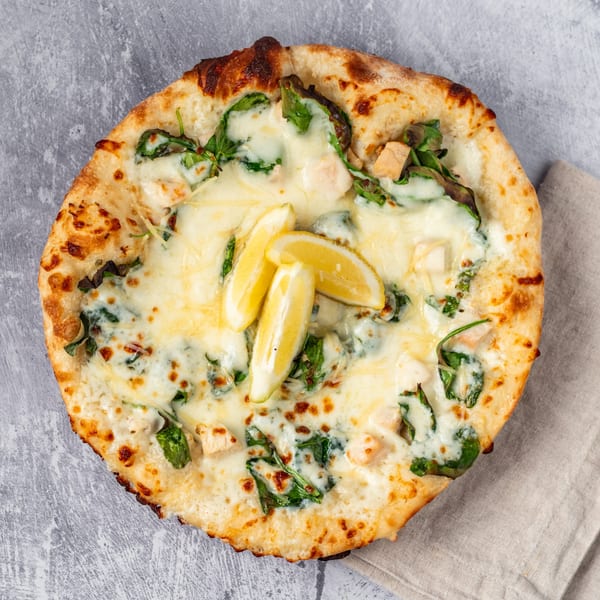 Pacioni's Pizzeria white pizza with spinach, chicken, and lemon slices on a gray surface.