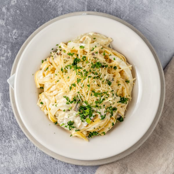 Creamy fettuccine alfredo with grated Parmesan cheese and fresh parsley in a white bowl.
