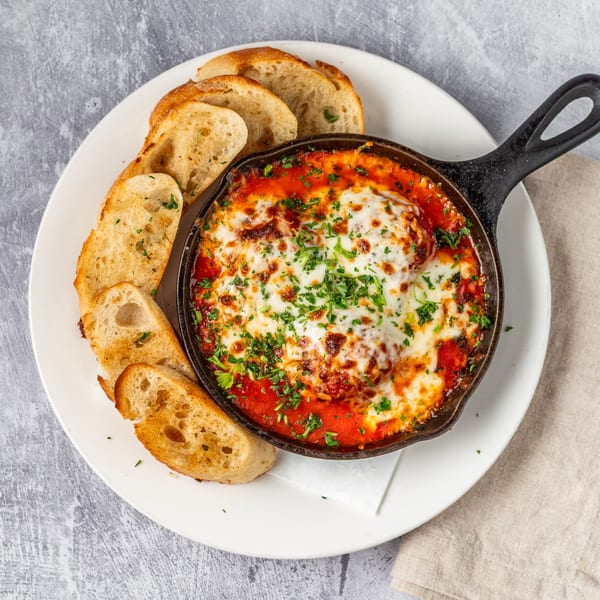 Pacioni's Pizzeria's baked meatballs in a cast iron skillet with melted cheese and toasted bread.