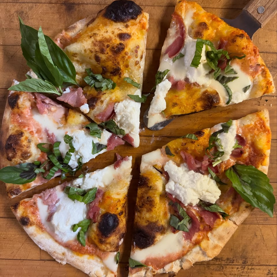 A Pacioni's Pizzeria pizza, cut into slices, topped with prosciutto, ricotta, and basil.