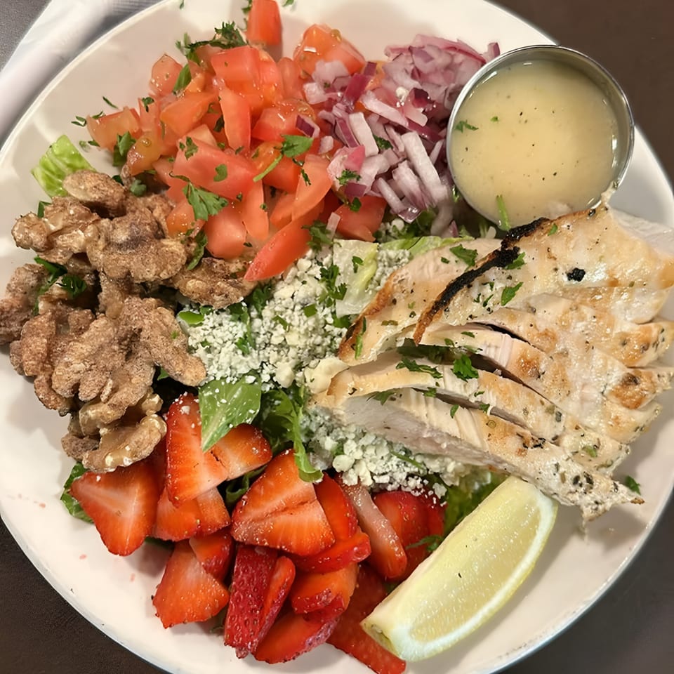 A vibrant salad with grilled chicken, strawberries, walnuts, tomatoes, red onion, and dressing.