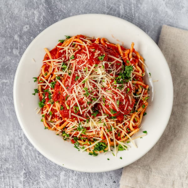 Spaghetti with meatballs, marinara sauce, grated Parmesan cheese, and fresh parsley in a white bowl.